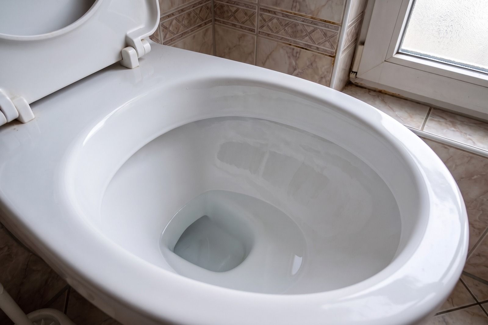 Dieselbe weiße Toilettenschüssel nach dem Spülen: saubere Keramik, klares Wasser, die Kante unter dem Rand frei von Streifen.